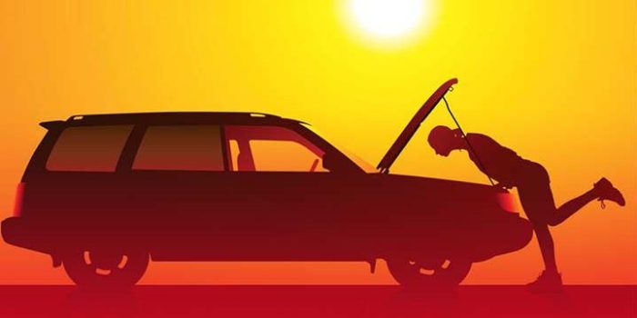 Silhouette of a person pushing a car with its hood up at sunset sunlit orange sky.