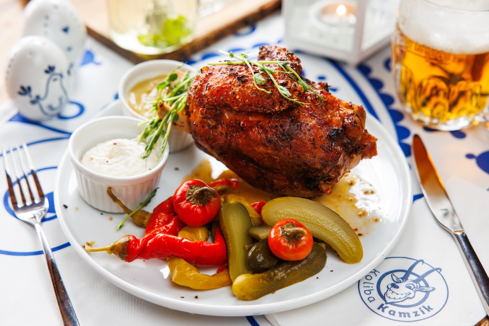 Plate with a roasted chicken leg, peppers, pickles, and two dipping sauces; beer in the background.