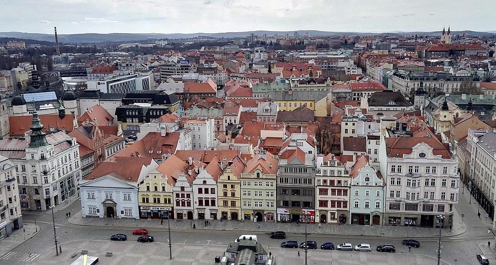 Aerial view of a European city with pastel-colored, gabled houses lining a wide street below.