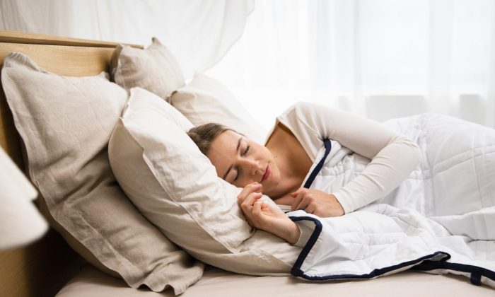 Woman sleeping on a bed with beige pillows and white quilt in a bright room, peacefully resting.